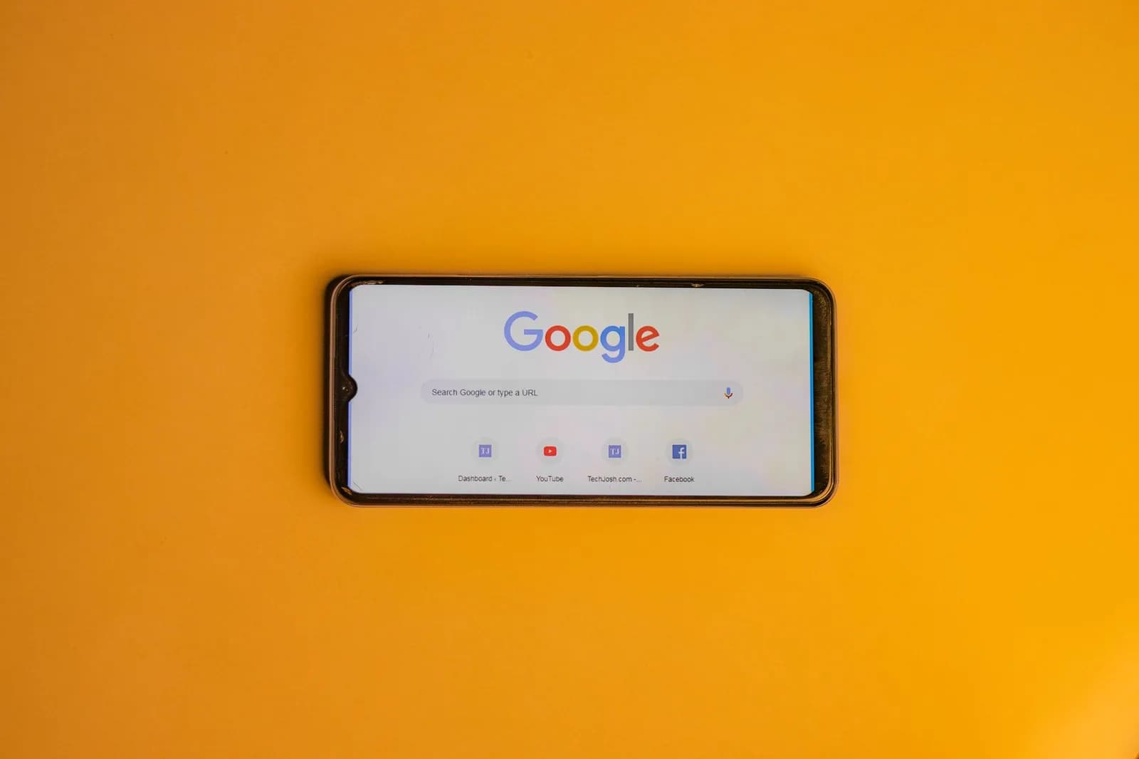 Smartphone displaying Google search page on a vibrant yellow background.